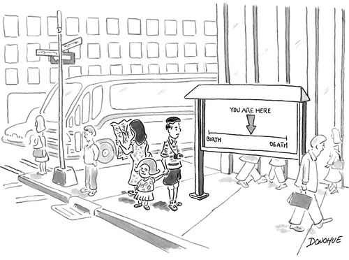 A man stands looking at a sign that shows a timeline labeled "Birth" and "Death" at opposite ends and an arrow pointing to the middle of the line labeled "You are here".