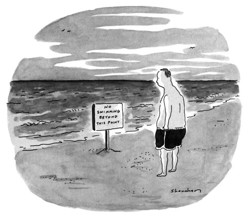 A man on a beach looks at a sign in front of the water that reads "No swimming beyond this point".