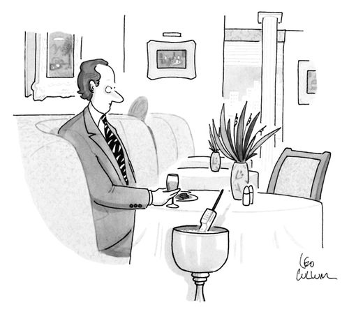 An angry looking man is sitting at a table in a restaurant; a cellphone is sitting in the wine bucket beside him.