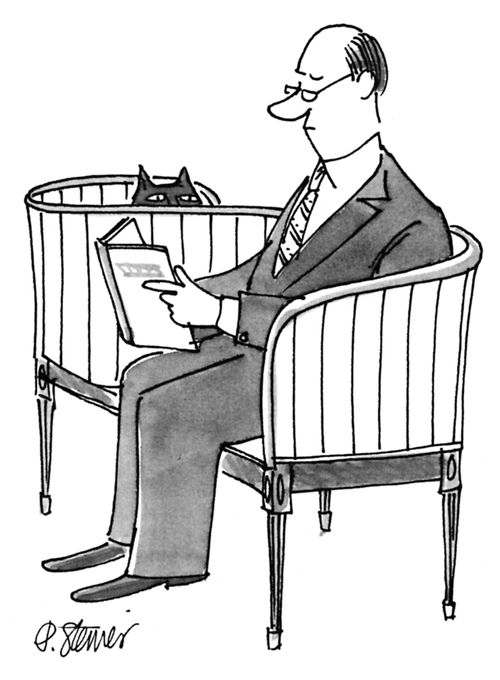 Man reads a book while seated in a loveseat as a cat peers over the seat at him. 