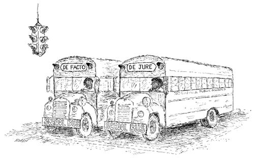 Two school buses are parked beside one another; one reads "De Facto" while the other reads "De Jure".
