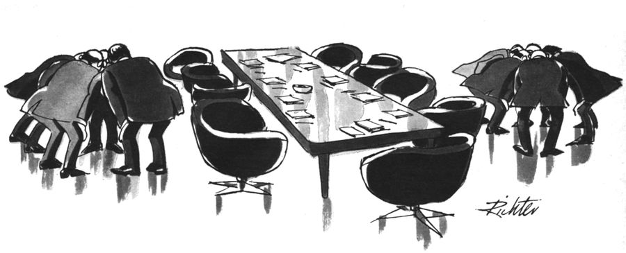 A meeting room with two teams of businessmen in huddles on opposite sides of the room.