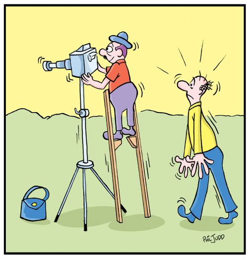 Short man standing on stilts to take a picture with a camera on a tripod.