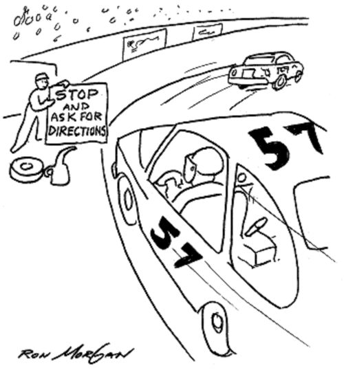 Racing pit crew member holds sign for driver: Stop And Ask For Directions.