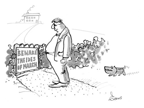 A man reads a sign saying 'Beware the Ides of March' is approached from behind by a small dog wearing a coat which reads 'Ides'.