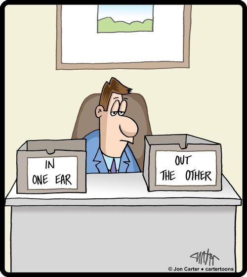 Business man sitting at desk with inbox and outbox reading 'In one ear,' and 'out the other.'