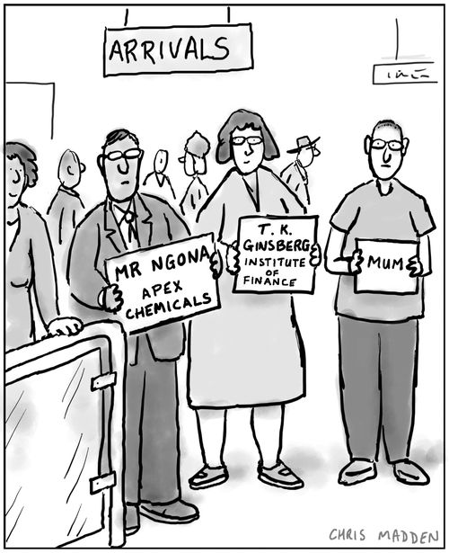 Young man holding a notice at an airport arrivals gate, reading 'Mum'.