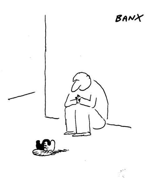 A man sits on a street corner with a toupee in front of him."